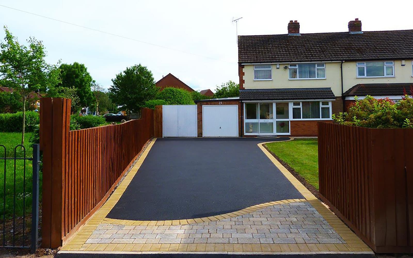 Front driveway with crisp black asphalt, buff brick edging, and timber fencing